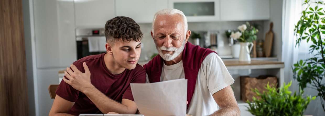 Grootvader en kleinzoon bestuderen samen thuis financiële documenten.